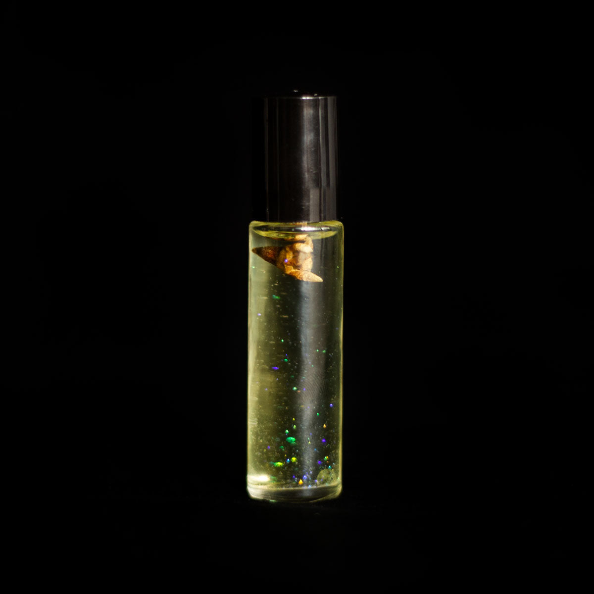 A perfume vial filled with pale yellow oil, containing a Geraldton Wax flower, a small peridot crystal chip, and bio-glitter
