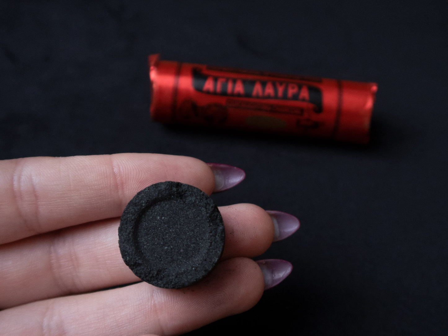 Fingers holding a charcoal tablet (for scale - it it slightly narrower than two fingers)