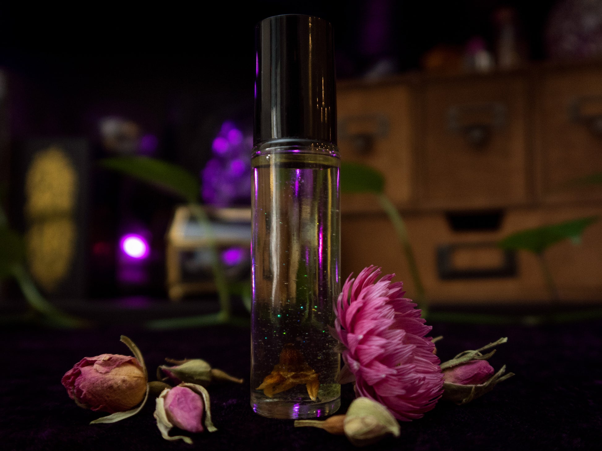 A perfume vial filled with pale yellow oil, containing a Geraldton Wax flower, a small peridot crystal chip, and bio-glitter