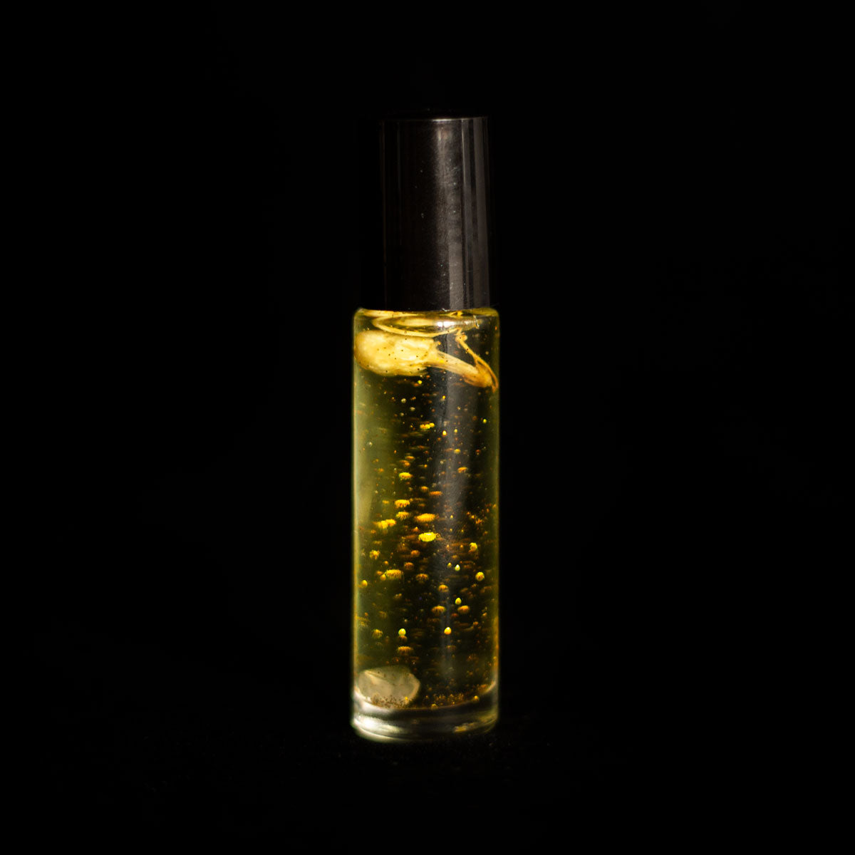 A perfume vial filled with pale yellow oil, containing a jasmine flower, a small rose quartz crystal chip, and bio-glitter