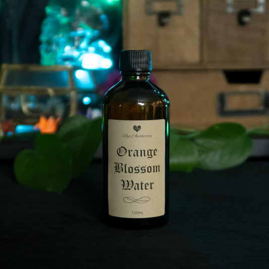 An amber glass bottle with a screw cap and antique-style label reading "Orange Blossom Water"