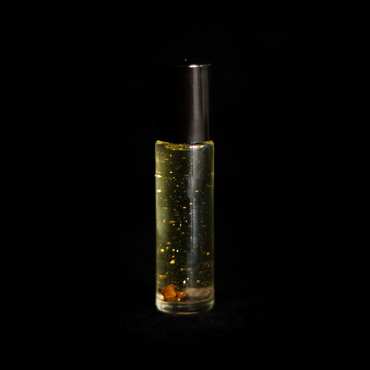 A perfume vial filled with pale yellow oil, containing a clove bud, a small amethyst crystal chip, and bio-glitter