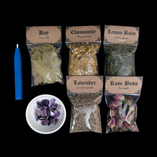 A blue chime candle, small bowl of large amethyst crystal chips, and 5 bags of herbs with Victorian-apothecary-style brown labels at the top give the common and Latin names