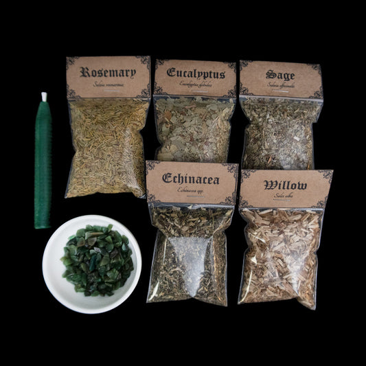 A green chime candle, small bowl of green aventurine crystal chips, and 5 bags of herbs with Victorian-apothecary-style brown labels at the top give the common and Latin names