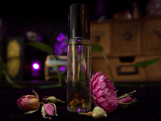 A perfume vial filled with pale yellow oil, containing a Geraldton Wax flower, a small peridot crystal chip, and bio-glitter